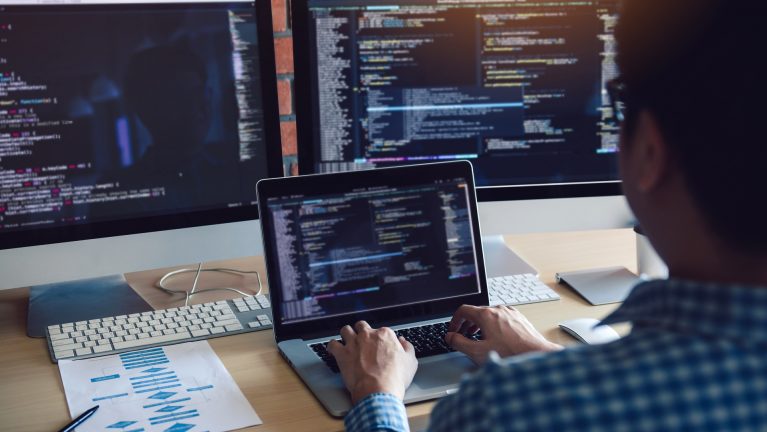 Rear view of software developers is sitting serious analyzing data on the computer screen.